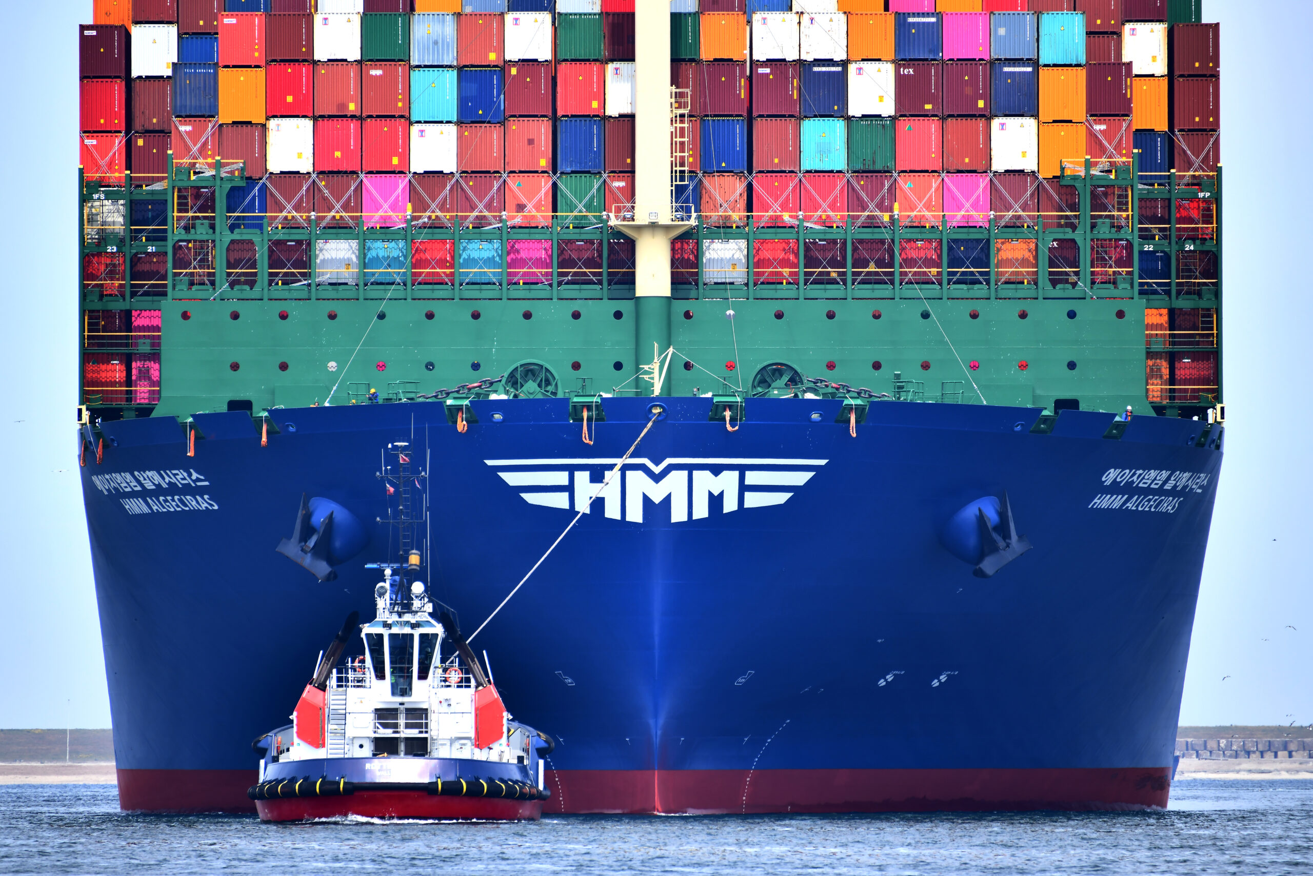 Schip met containers wordt door een sleeper de Rotterdamse haven in geloodst.